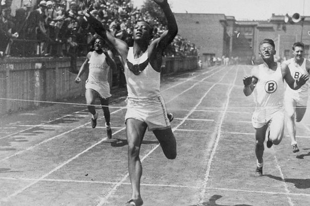 Cleveland high school student and future Olympic champion Jesse Owens (1913 - 1980) holds his hands in the air while crossing a finish line to break the world 100-meter record